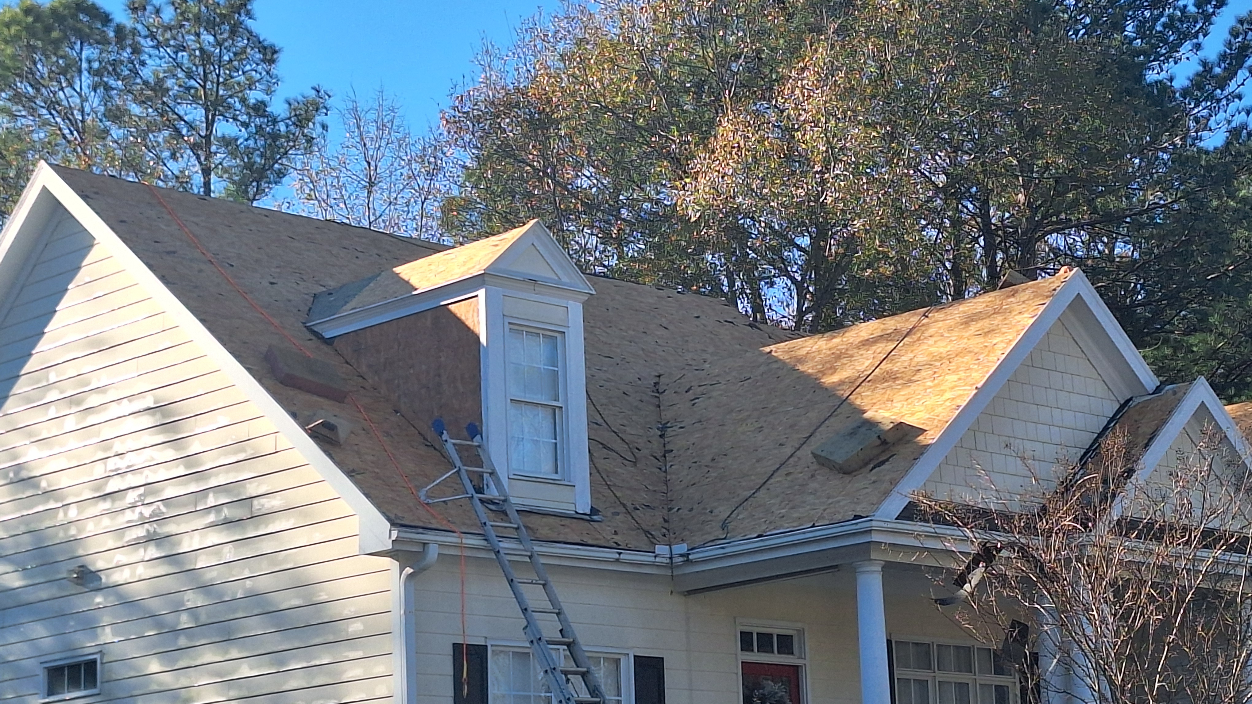 Roof repair in progress with ladder against white house under blue sky